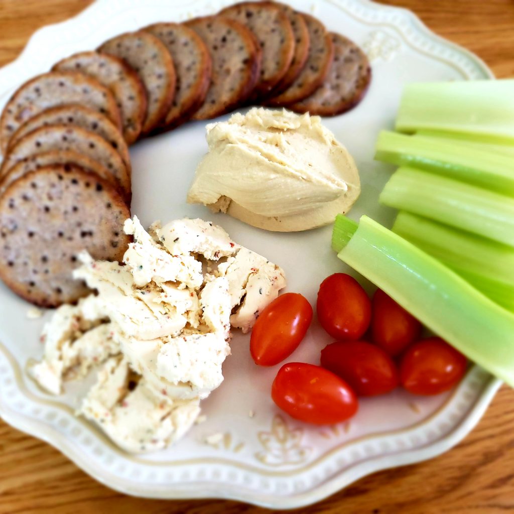 plate with crackers, cheese, hummus, tomatoes, celery