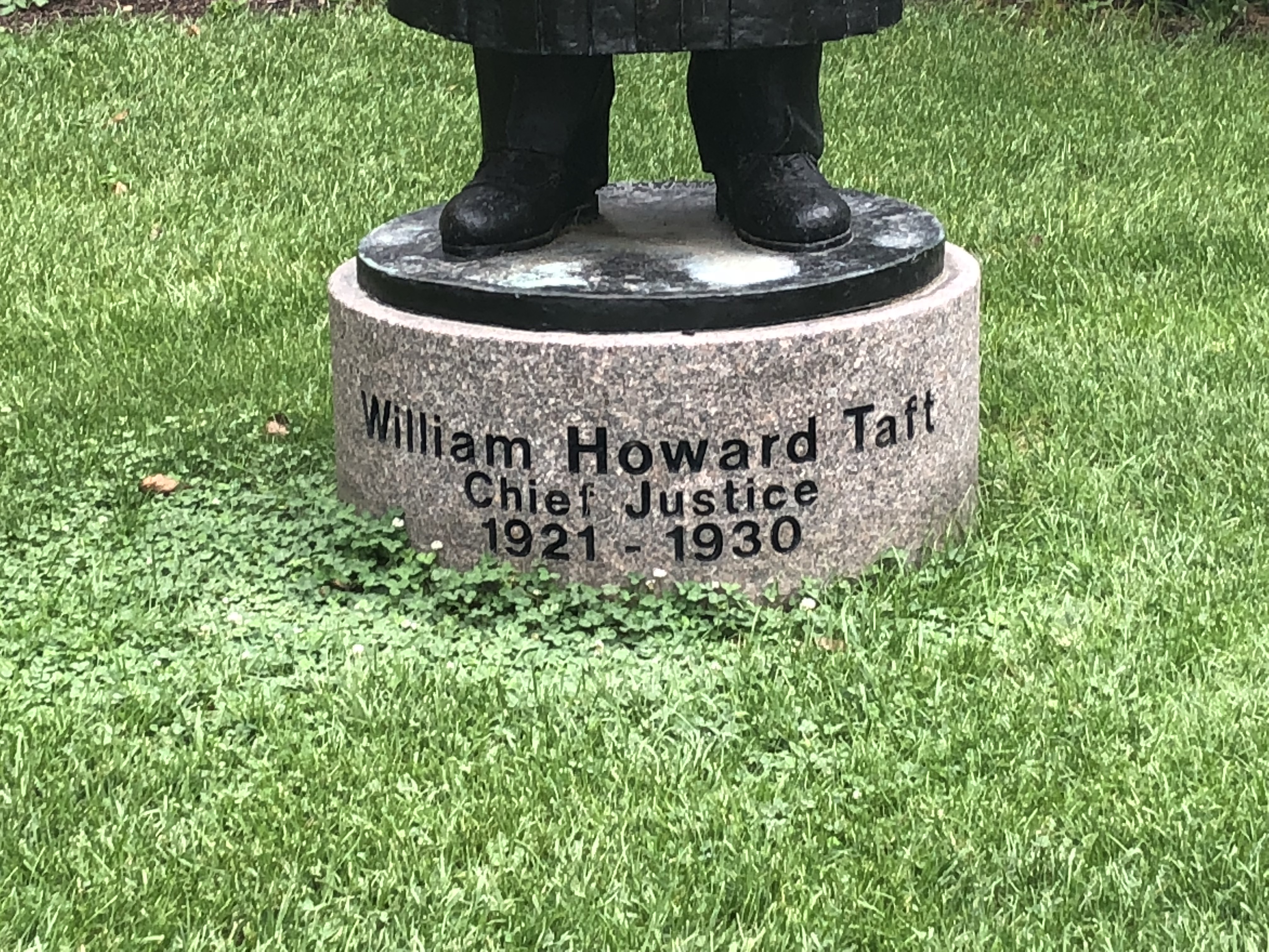 Photograph of base of William Howard Taft statue in grass.