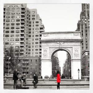 A black and white photo of Washington Square PArk, with a girl wearing red.
