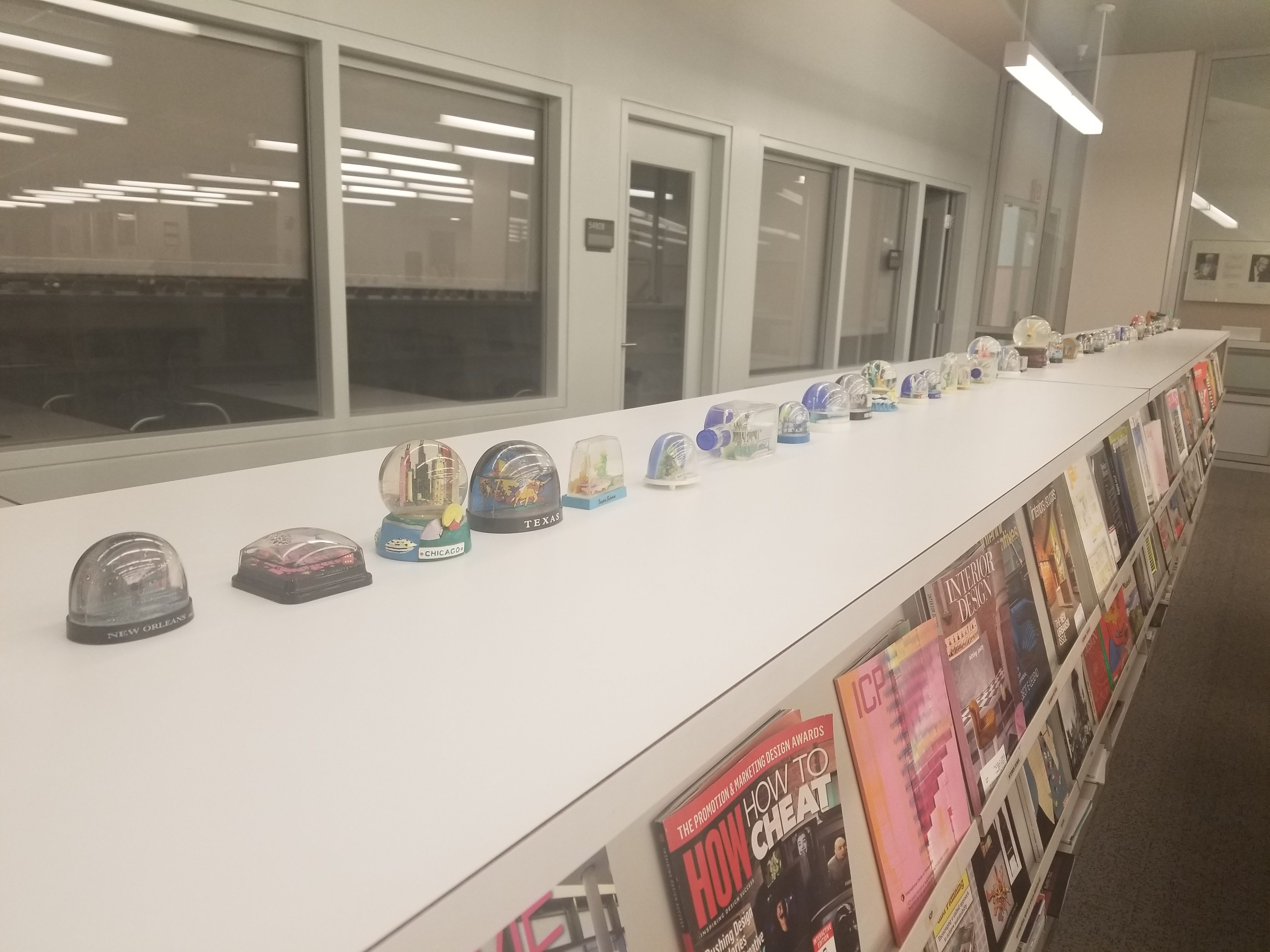 Line of snow-globes on a bookshelf in the DAAP Library