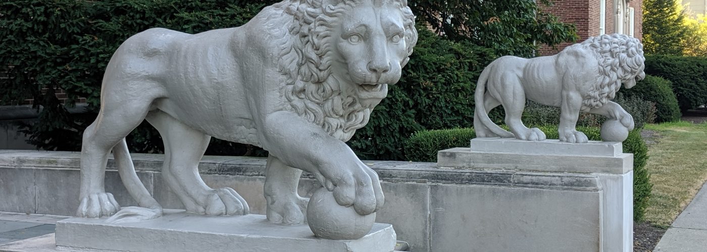 two stone lions along stairs in front of a red brick building