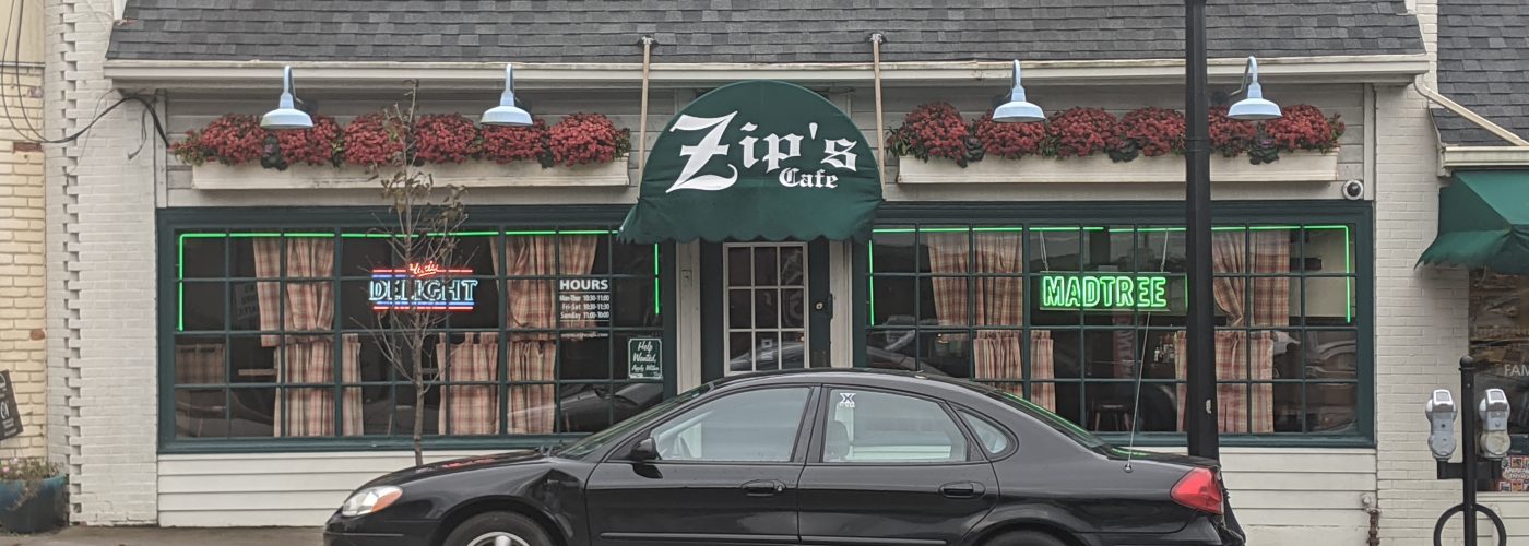 storefront with green zips sign and a black car parked out front