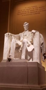 The Lincoln Memorial in Washington DC. Its a large white marble monument of Abraham Lincoln sitting in a chair with a quote behind him.