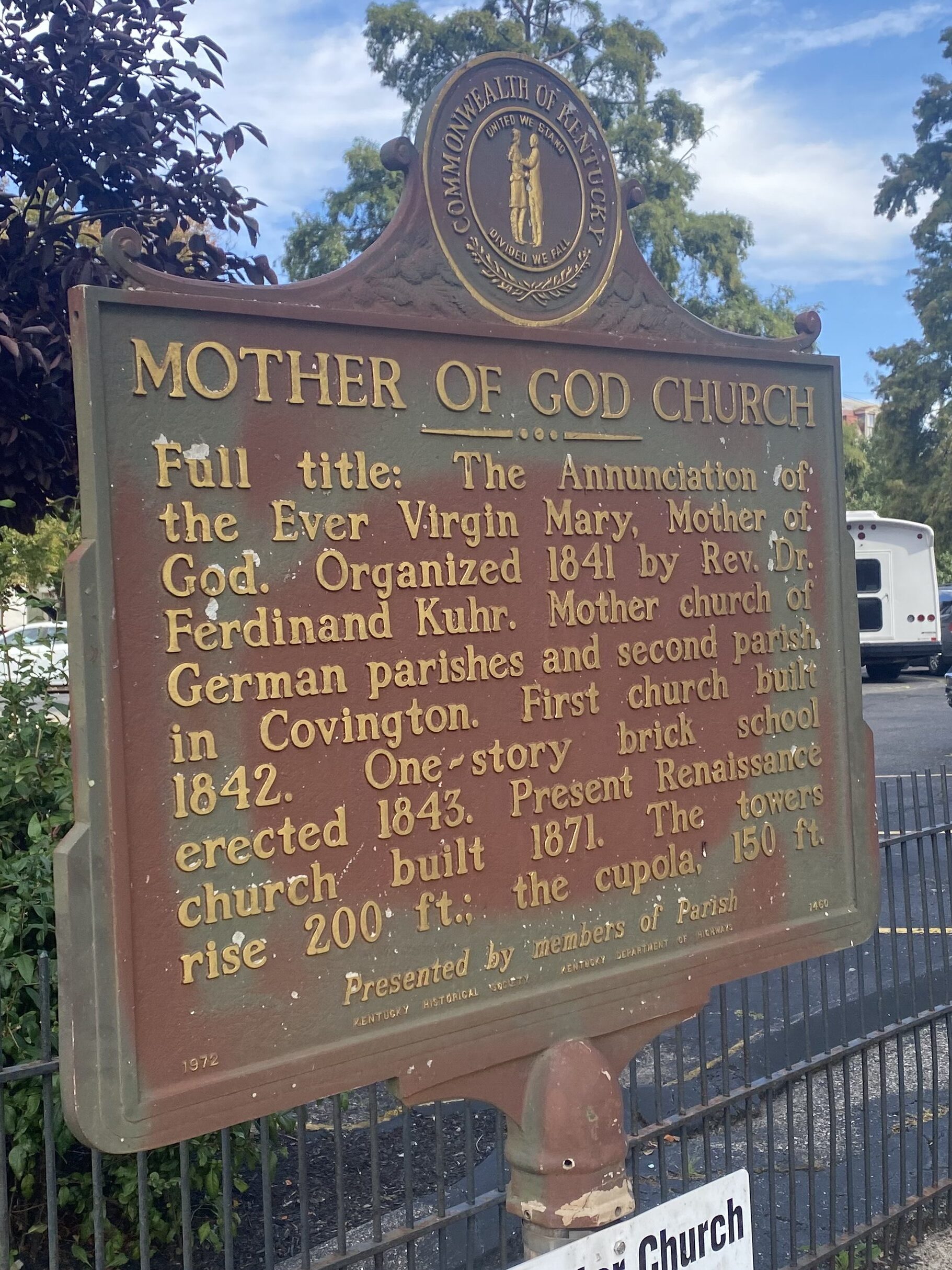 Sign with title "Mother of God Church" and text reading "Full title: The Annunciation of the Ever Virgin Mary, Mother of God. Organized 1841 by Rev. Dr. Ferdinand Kuhr, Mother church of German parishes and second parish in Covington. First church built 1842. One-story brick school erected in 1843. Present Renaissance church built 1871. The towers rise 200 ft.; the cupola 150 ft."