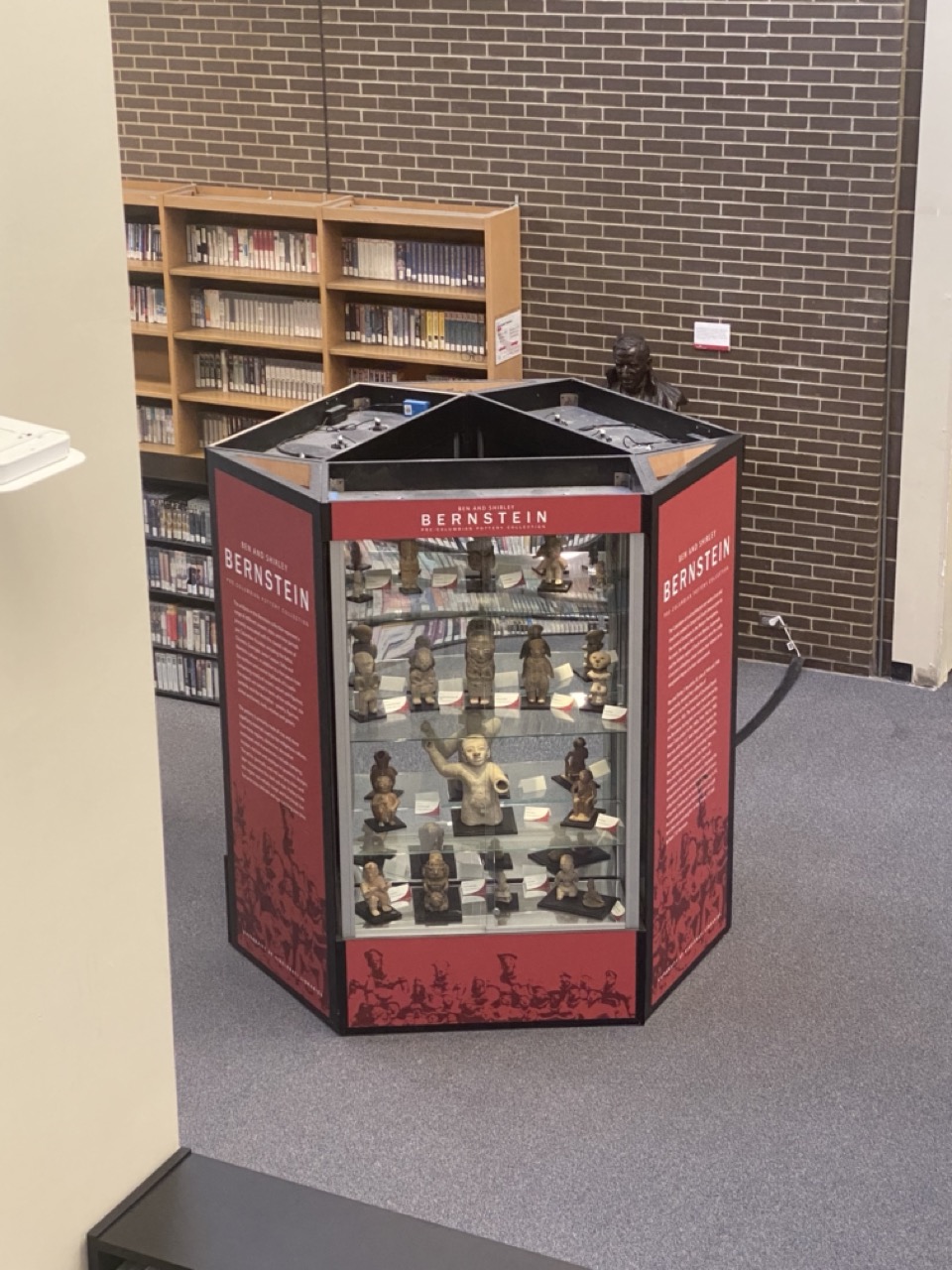 Six-sided installation of 3 glass cases holding replicas of Ecuadorian pottery and 3 sides of texts on red walls