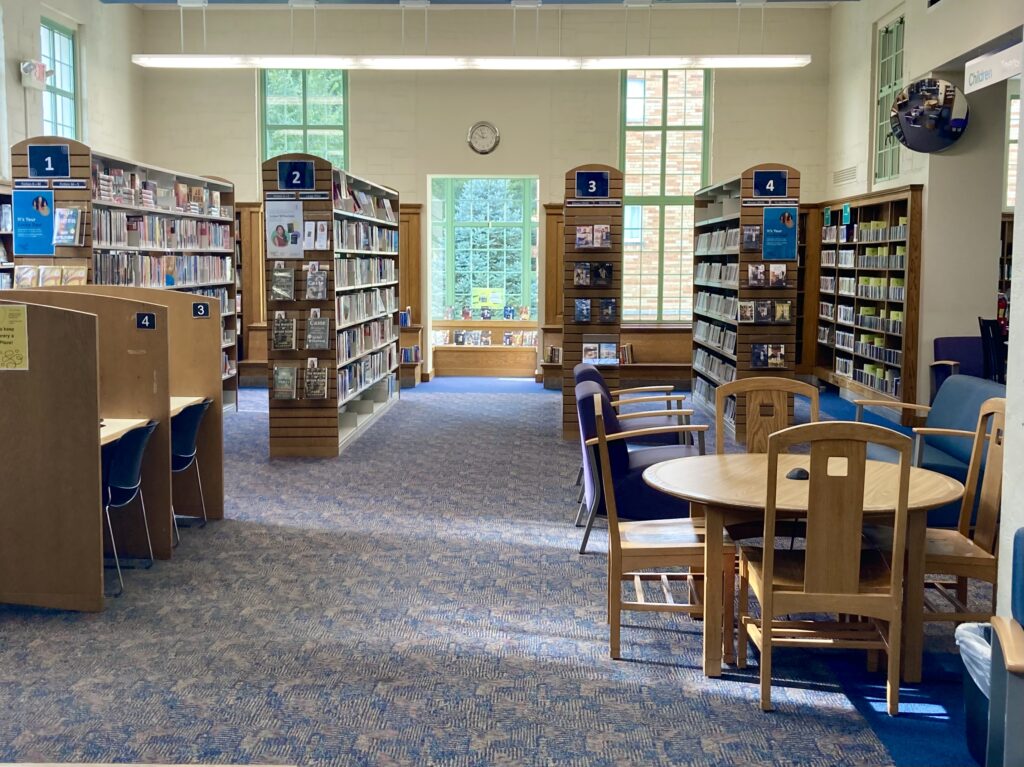 Inside a library, featuring couches, desks, tables, and four rows of bookshelves.