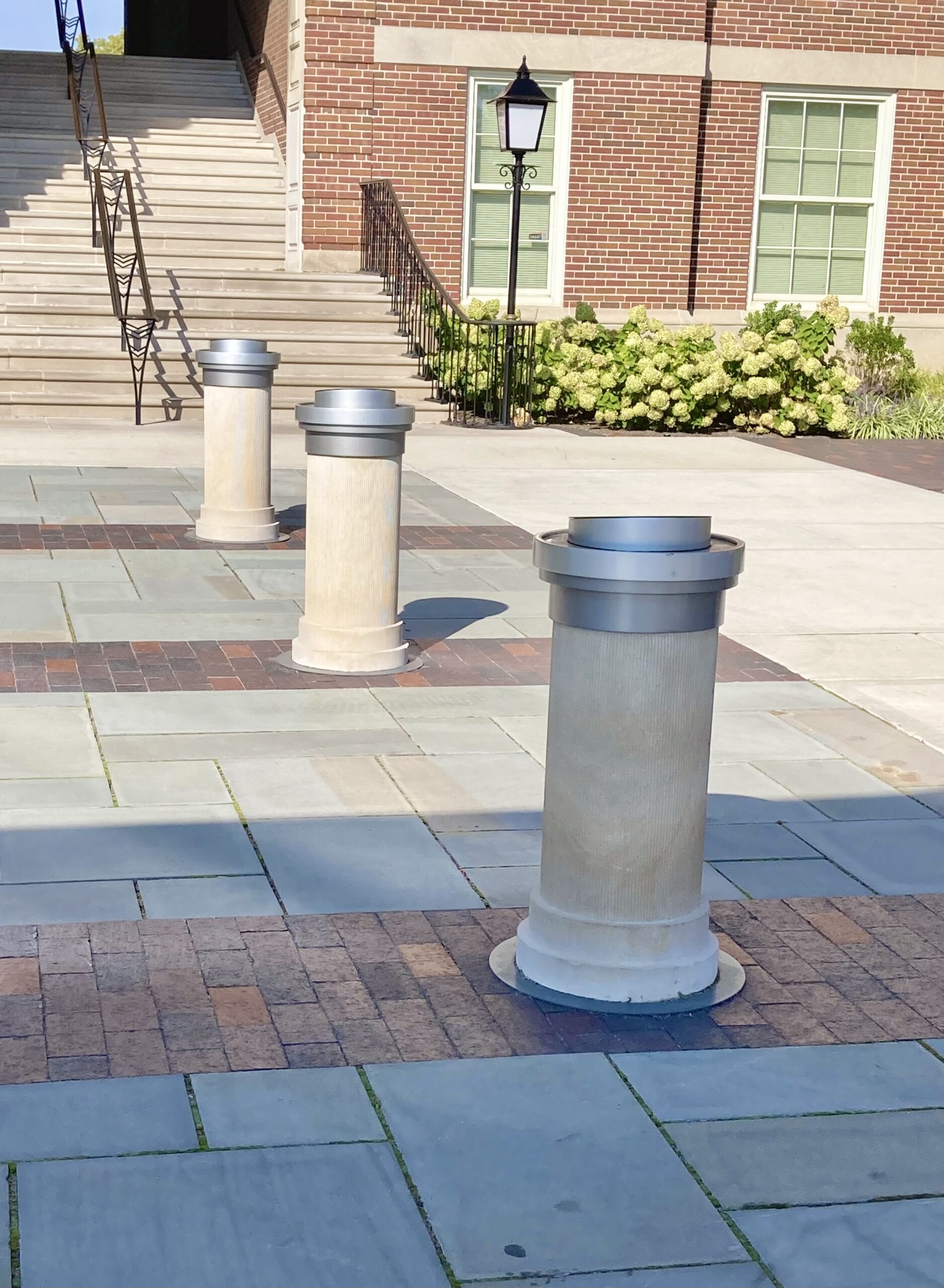 Three stone columns on pavement outside a brick building.