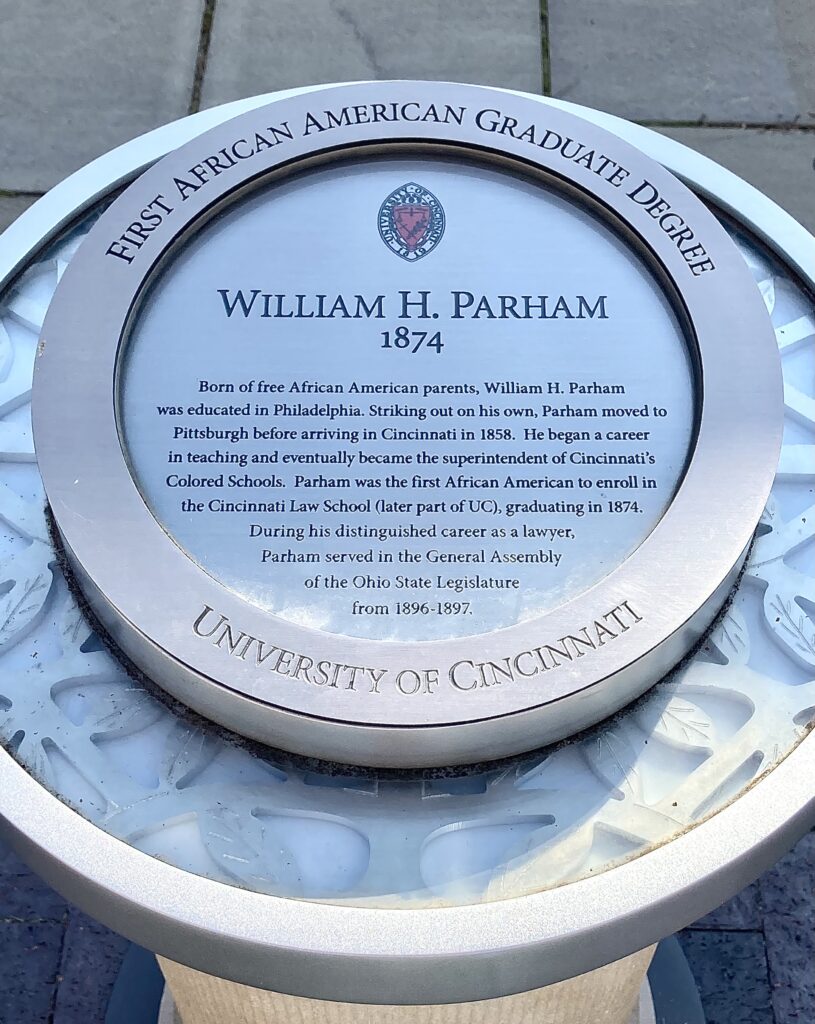 A round metal plaque with text. The words "William H. Parham, 1874" are centered on the plaque.