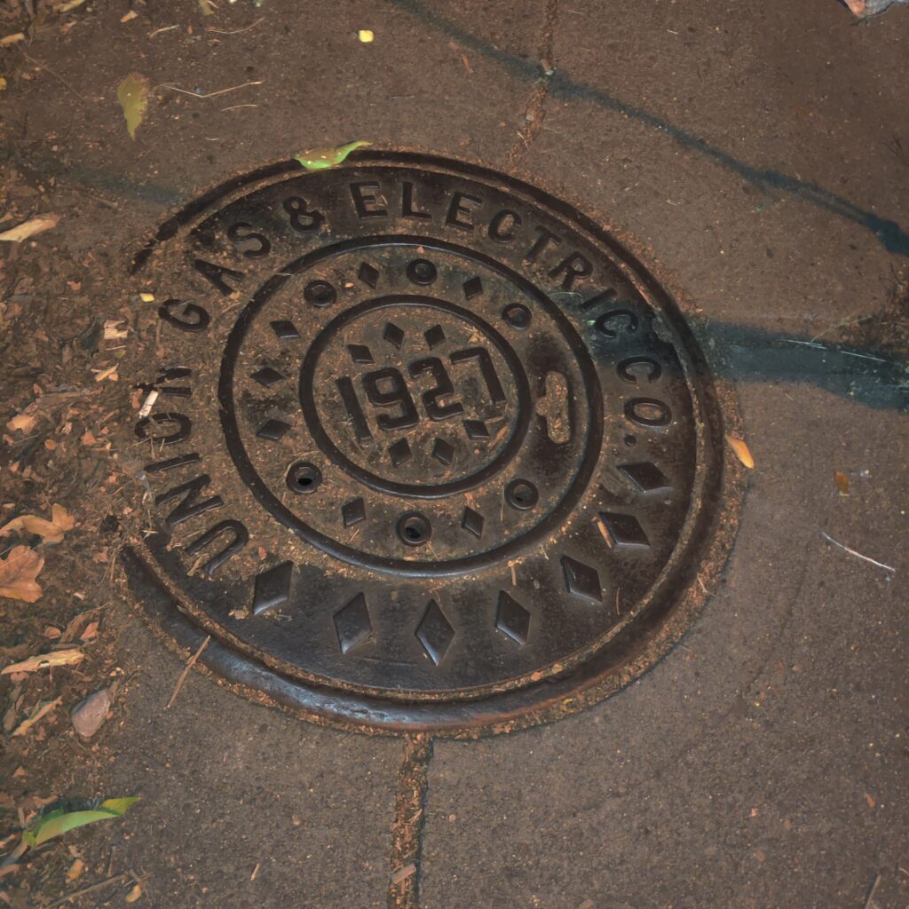 Metal manhole cover for the Union Gas and Electric Company on the sidewalk, dated 1927.