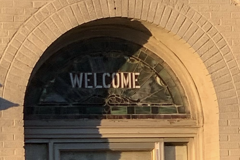 Original stained glass entrance transom window with the word "WELCOME" incorporated into the design with milk glass, fall 2023.