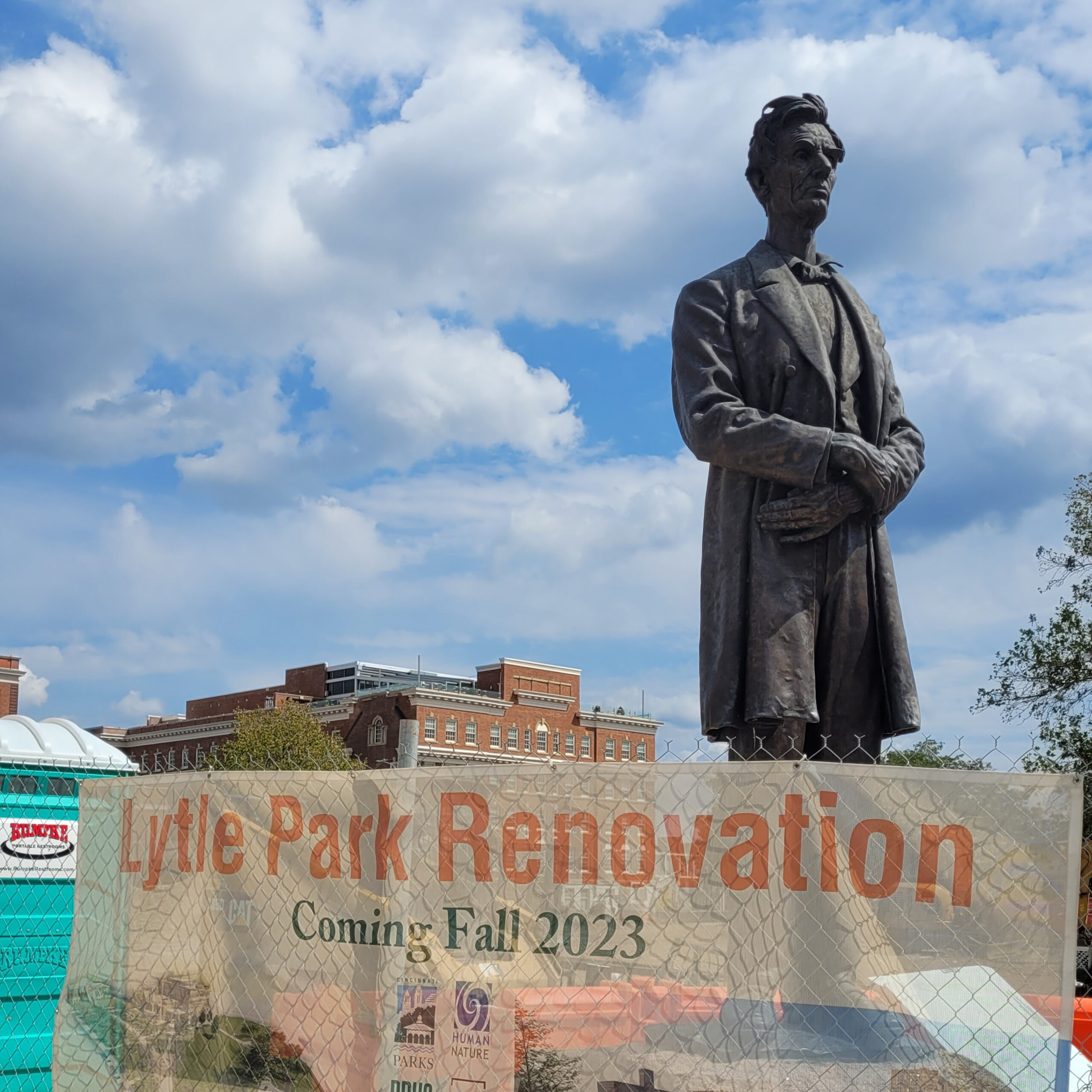 The majority of a statue of Abraham Lincoln is visible above a chain link fence with a sign reading "Lytle Park Renovation: Coming Fall 2023"