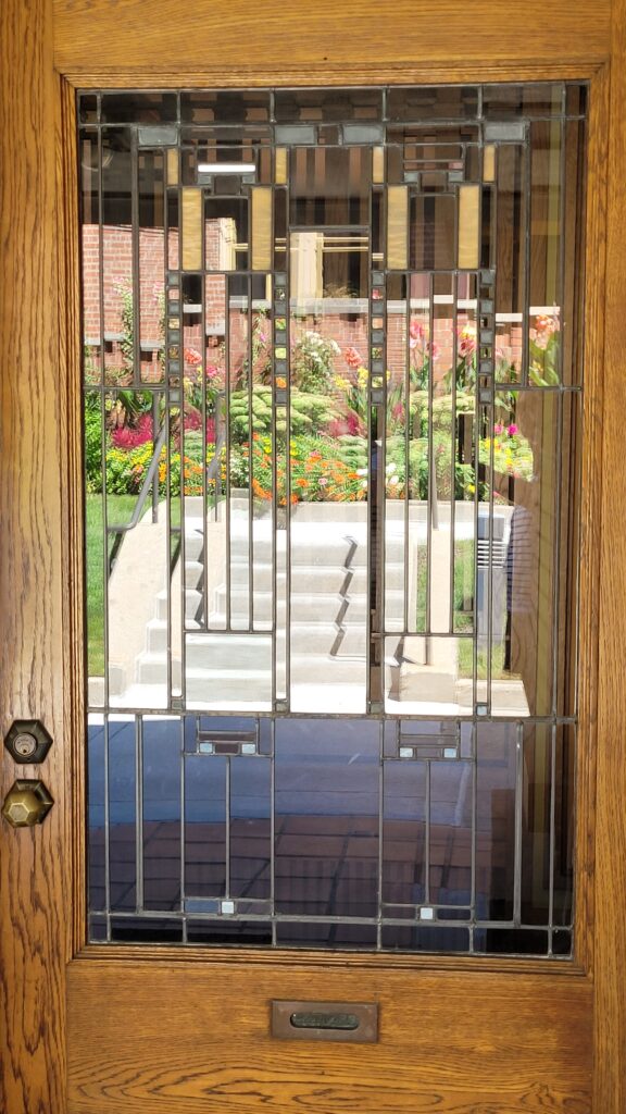 A wooden door with art deco style leaded glass window reflecting the outside landscaping