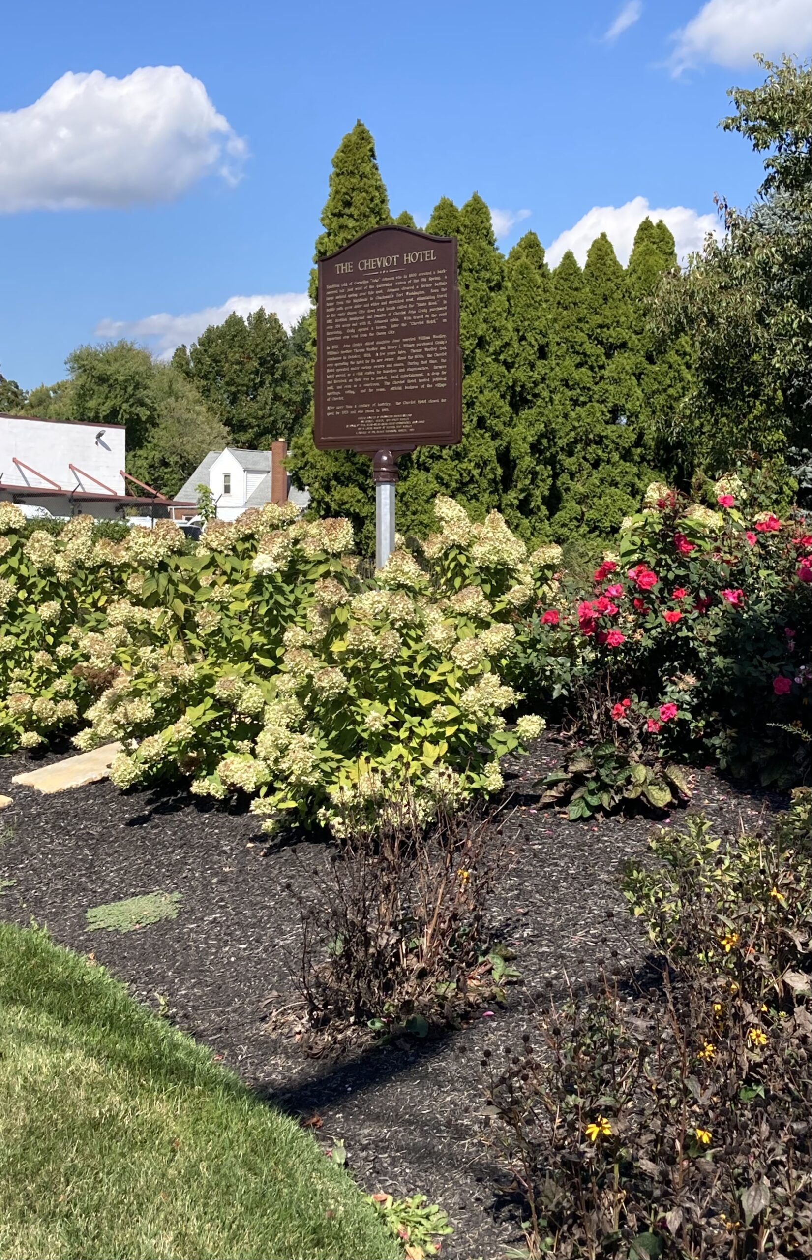 A brown sign surrounded by flower bushes.