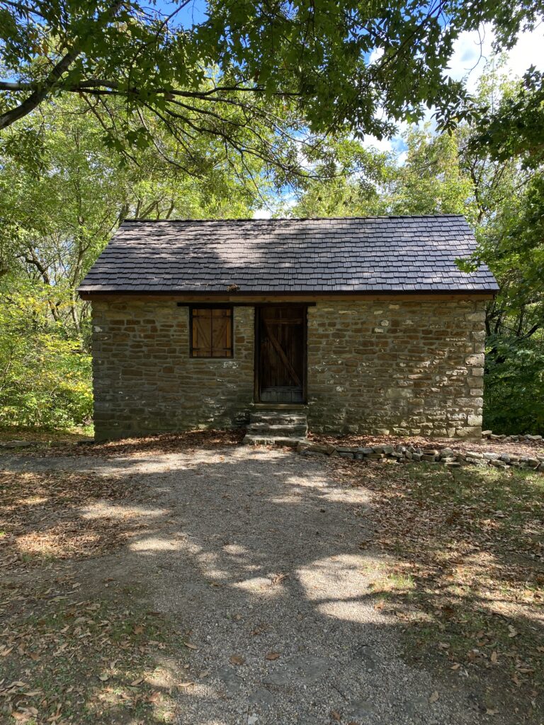 The top story of a stone brick schoolhouse with one window and a wooden door.