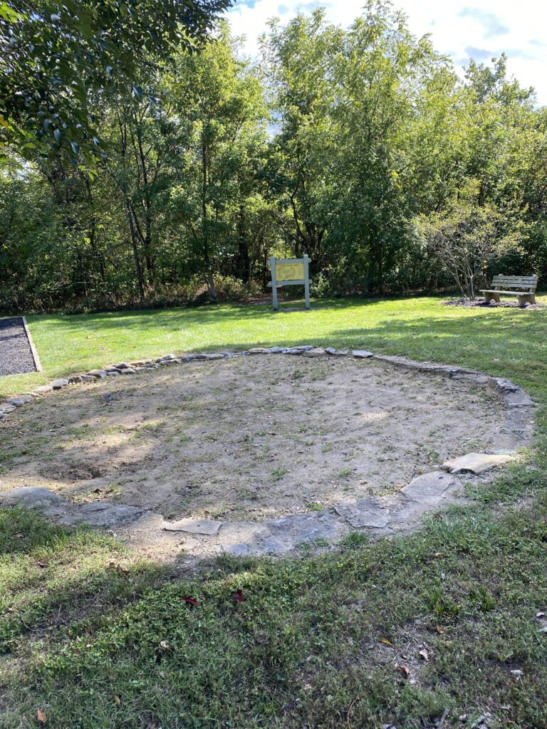 A stone-lined pit that has been filled in with dirt in the middle of the park
