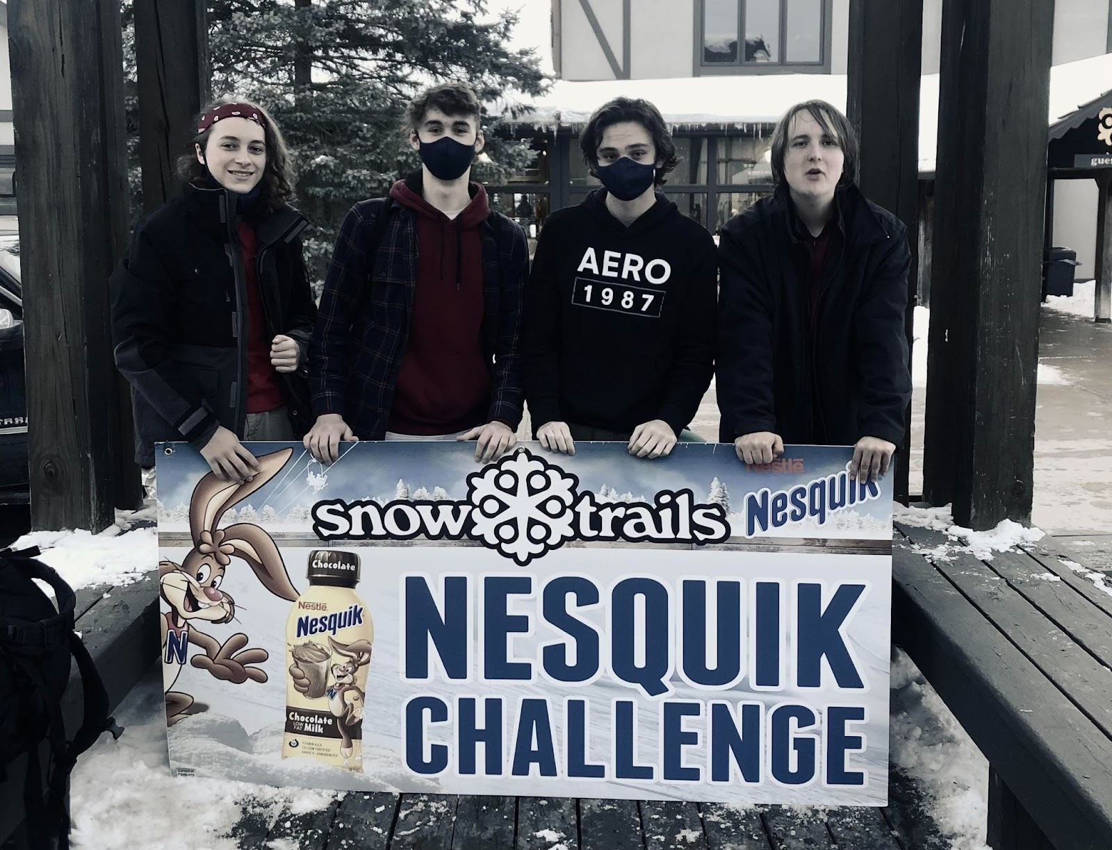 young men standing behind a nesquik sign